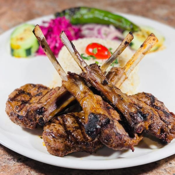 Grilled lamb chops and ribs with rice, red cabbage, and green pepper on a white plate.