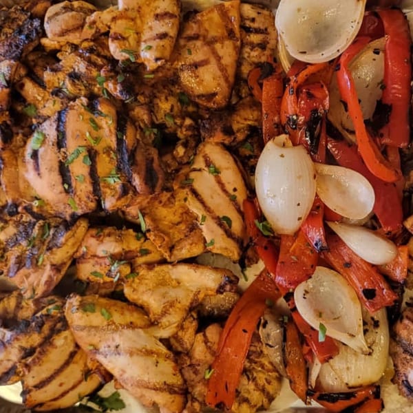 Grilled chicken pieces with char marks, garnished with parsley, alongside grilled red peppers and onions.