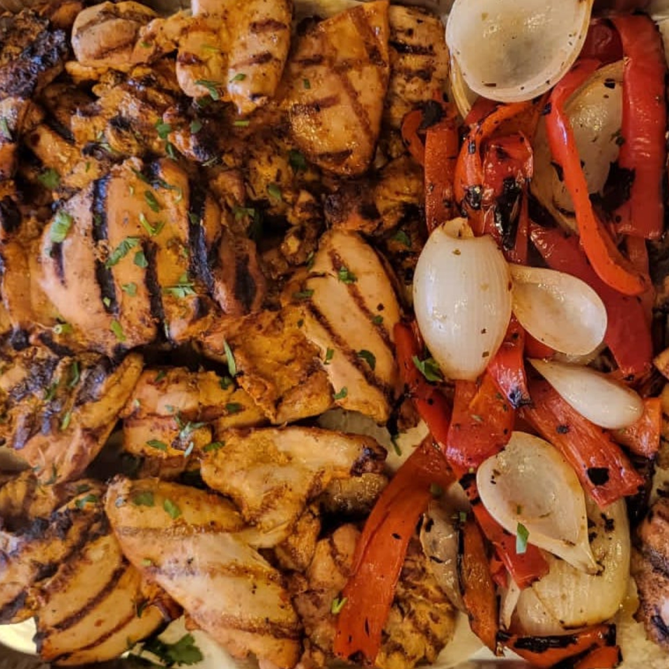Grilled chicken pieces with char marks, garnished with parsley, alongside grilled red peppers and onions.