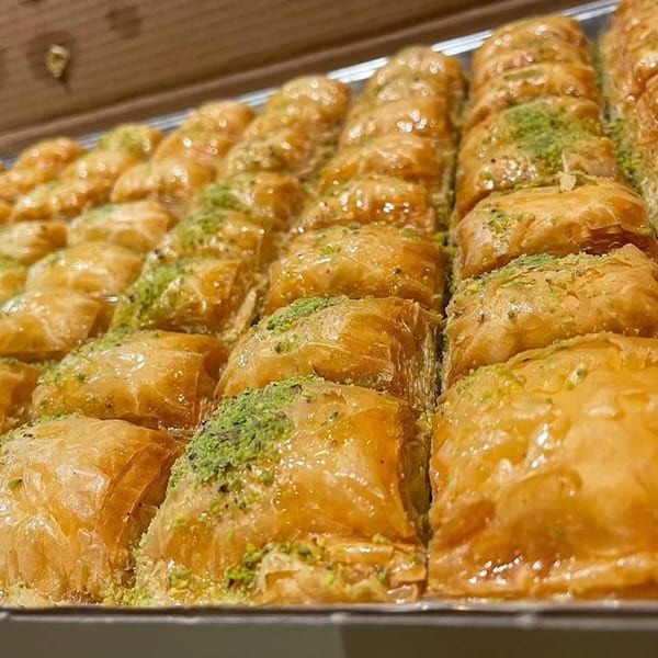 Rows of golden, glistening baklava squares topped with chopped pistachios in a tray.