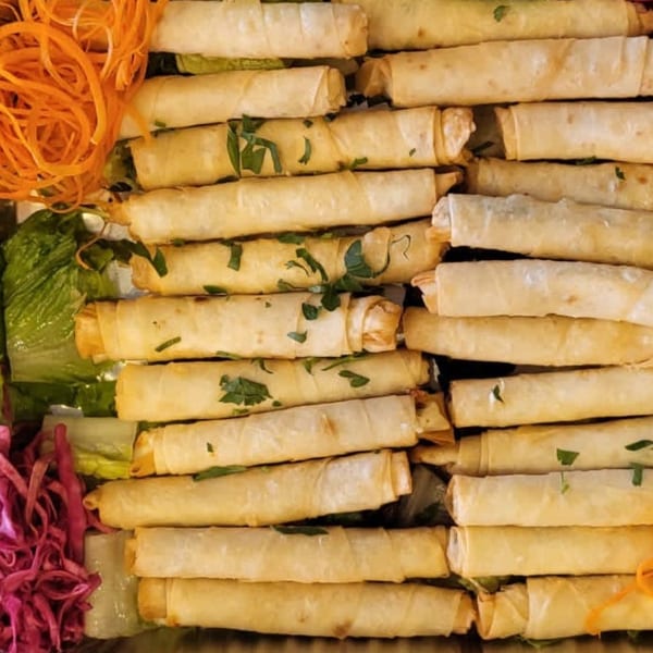 Crispy golden Mediterranean spring rolls, garnished with fresh parsley, shredded carrots, and red cabbage.
