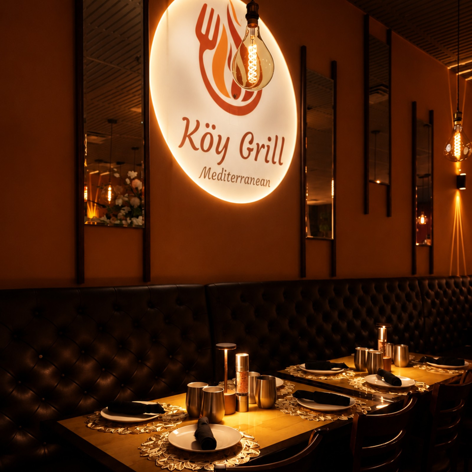 Warmly lit Kōy Grill Mediterranean restaurant interior with tufted leather seating, set tables, and glowing pendant lights.