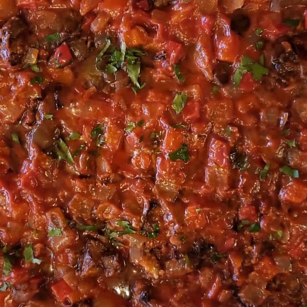 Close-up of a rich, red Mediterranean stew with chopped vegetables and herbs.
