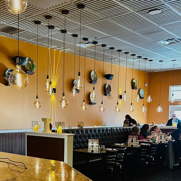 Koy Grill's dining area features warm orange walls, hanging Edison bulbs, and patrons seated at black booths.