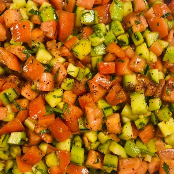 Close-up of a vibrant Mediterranean salad with diced tomatoes and cucumbers, seasoned with herbs.