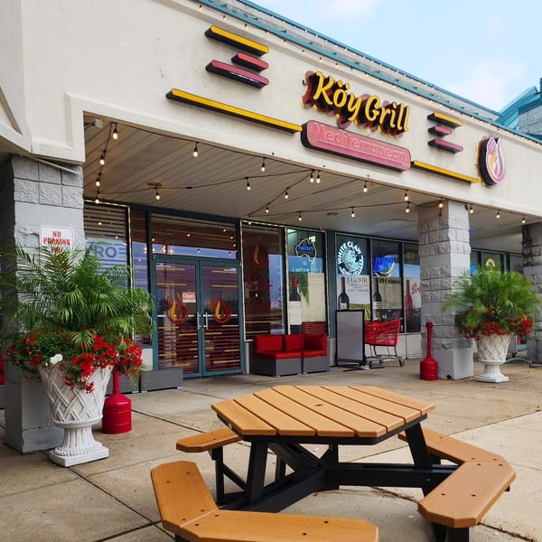 Exterior of Koy Grill Mediterranean restaurant with a picnic table and string lights outside.