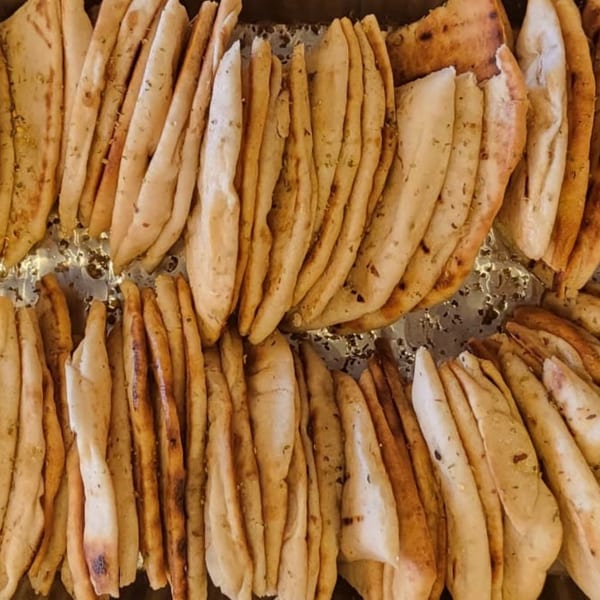Rows of freshly baked, warm Mediterranean flatbreads, some with visible herbs, ready to be served.