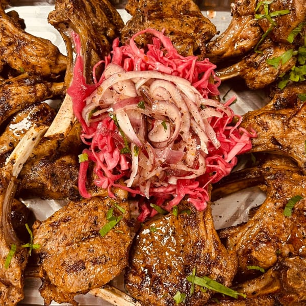 Grilled lamb chops with pickled red cabbage and onions, garnished with fresh herbs.