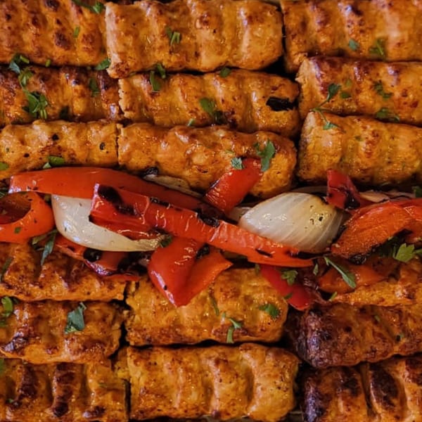 Rows of grilled Mediterranean chicken kebabs with charred red peppers and onions.