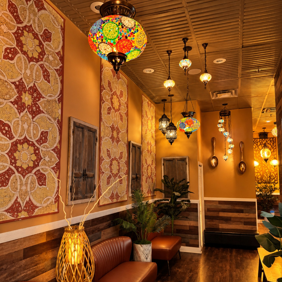 Warmly lit restaurant interior featuring colorful mosaic pendant lamps, patterned wall panels, wood accents, leather seating, and plants.
