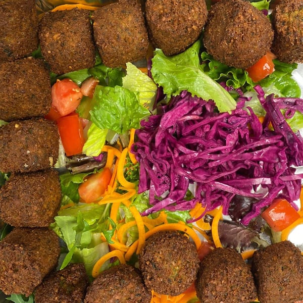 Crispy falafel balls arranged around a vibrant salad with lettuce, tomatoes, shredded carrots, and red cabbage.