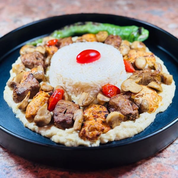 Koy Grill's Mediterranean dish with rice, grilled meats, mushrooms, and peppers on a dark plate.
