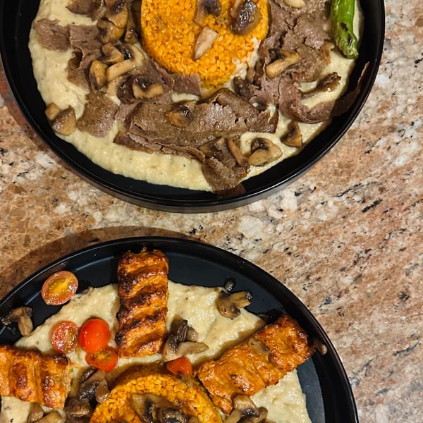Two Mediterranean dishes with meat, mushrooms, rice, and a creamy base on a speckled countertop.