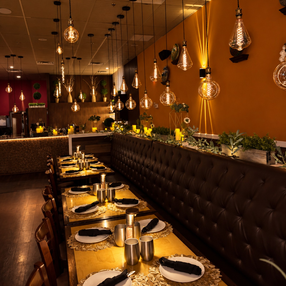 Warmly lit restaurant dining area with pendant bulbs, candlelit tables, leather banquette seating, and decorative plants.