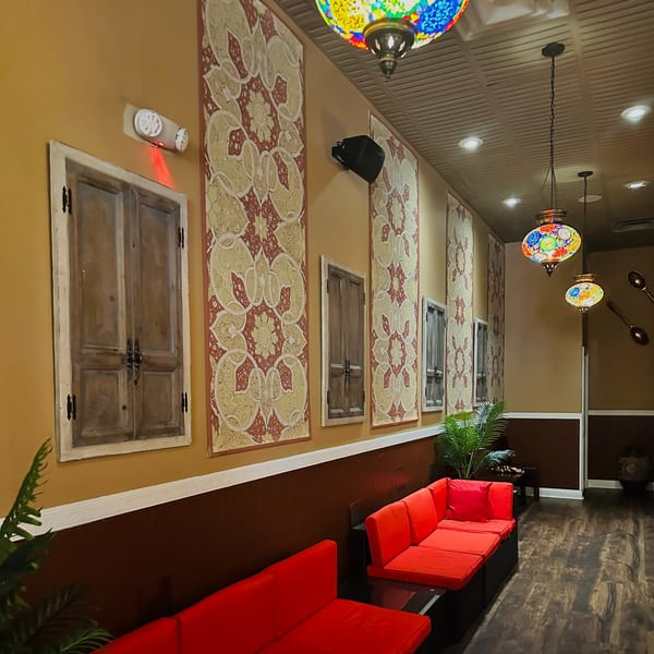 Mediterranean restaurant interior with red couches, patterned wall hangings, and colorful mosaic lamps.