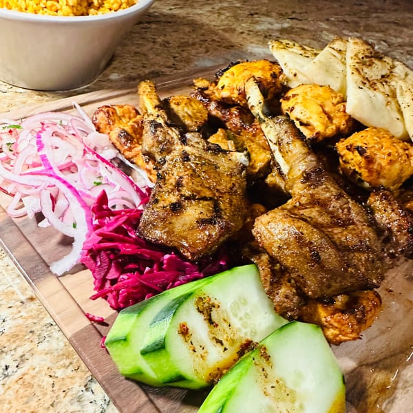 A Koy Grill platter with grilled lamb chops, chicken, pita, pickled onions, cabbage, and cucumbers.