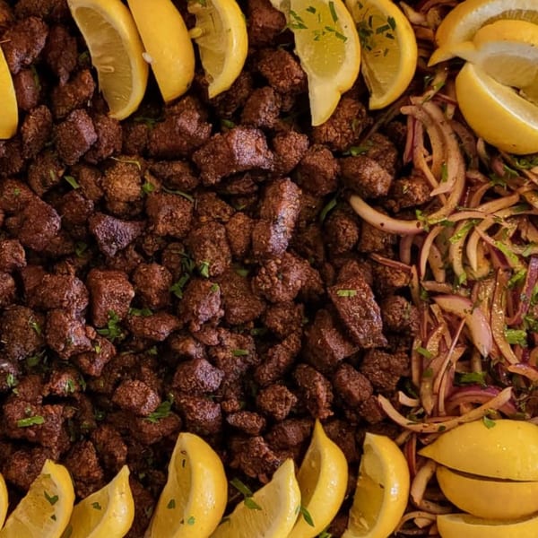 Close-up of Koy Grill's Mediterranean lamb liver with lemon wedges and red onions.