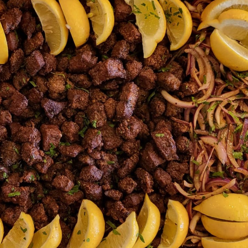 Close-up of Koy Grill's Mediterranean lamb liver with lemon wedges and red onions.
