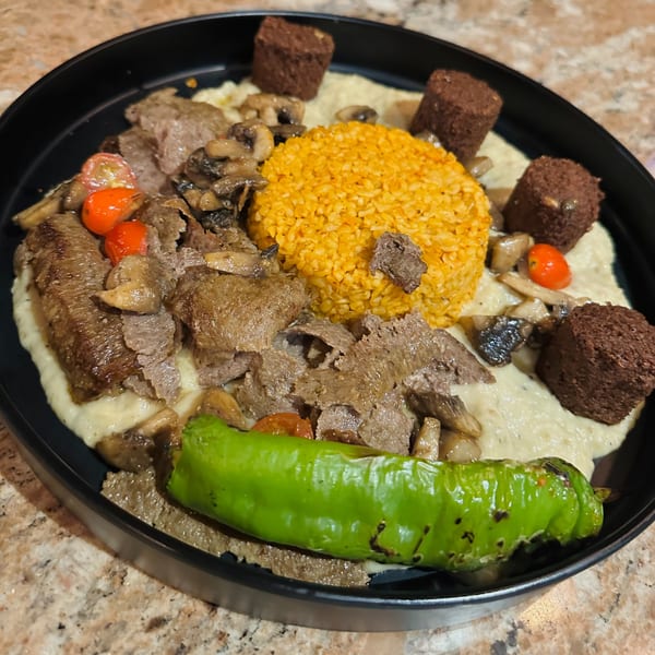 A Mediterranean dish with sliced meat, yellow rice, mushrooms, tomatoes, and a green pepper.