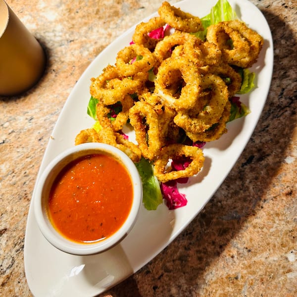 Crispy fried calamari rings on a bed of lettuce with a side of red dipping sauce.