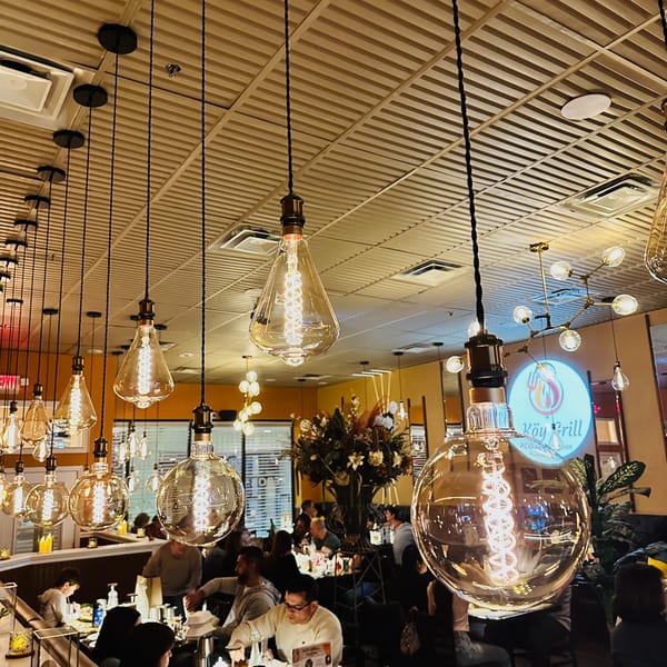 Warmly lit Koy Grill dining room with Edison bulb pendant lights and blurred patrons enjoying their meals.