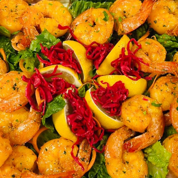 Koy Grill's Mediterranean shrimp dish with lemon wedges, red cabbage, and green lettuce.