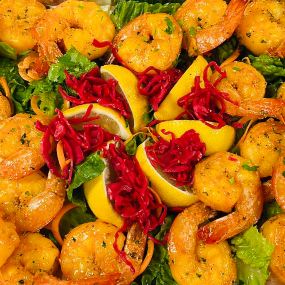 Koy Grill's Mediterranean shrimp dish with lemon wedges, red cabbage, and green lettuce.