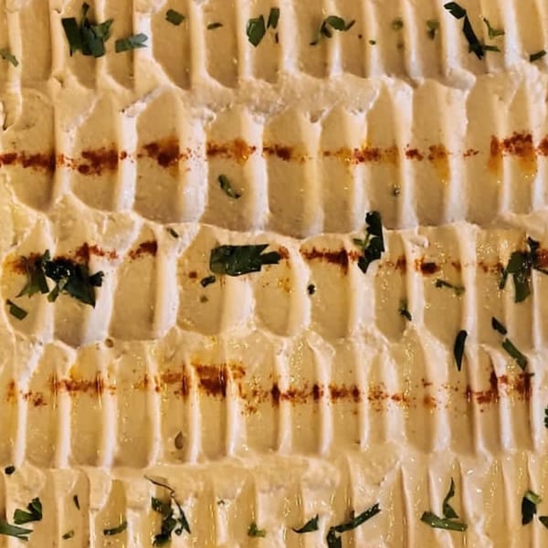 Close-up of creamy hummus with ridges, drizzled with olive oil, paprika, and fresh herbs.
