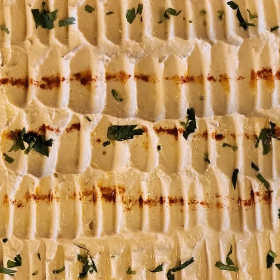 Close-up of creamy hummus with ridges, drizzled with olive oil, paprika, and fresh herbs.